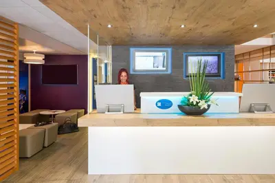 a woman standing behind a counter in a lobby at ibis budget Cannes Centre Ville in Cannes