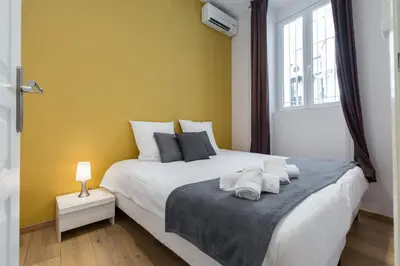a bedroom with a white bed with a yellow wall at Florella Marceau Apartment in Cannes