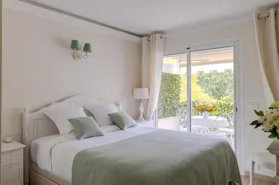 a white bedroom with a bed and a balcony at Appartement CANNES IMPERIAL Pointe Croisette in Cannes