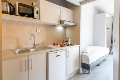 a kitchen with white cabinets and a sink and a bed at Zenitude Hôtel-Résidences Le Cannet in Le Cannet