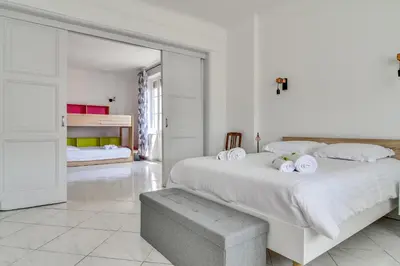a white bedroom with a large bed with white sheets at IMMOGROOM - Sea View - Balcony - 5 min from the beach - AC - Wifi in Cannes