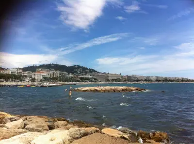 a beach with rocks in the water and buildings at New York 2 pièces 3 étoiles calme plein centre de cannes, 5mn des plages et Palais in Cannes