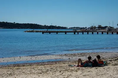 two people sitting on the beach near the water at Le Parc Pointe Croisette in Cannes