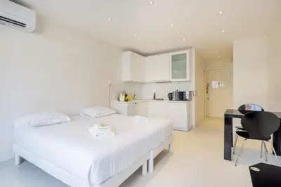 a white bedroom with a bed and a kitchen at Agence des Résidences - Appartements privés du 45 CROISETTE - Standard in Cannes