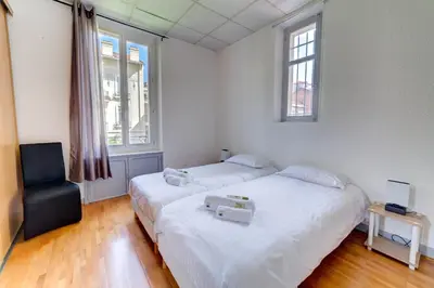 a bedroom with two beds and a chair and two windows at IMMOGROOM - Charming apartment - City Center - Wifi - AC in Cannes
