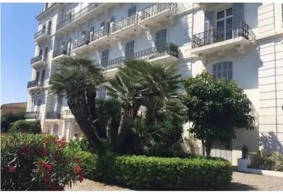 a large white building with palm trees in front of it at Winter Palace Cannes in Cannes