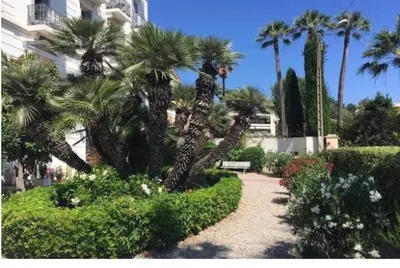 a garden with palm trees and a bench in front of a building at Winter Palace Cannes in Cannes