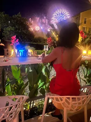 a woman in a red dress sitting at a table with fireworks at Winter Palace Cannes in Cannes