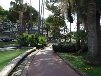 a walkway in a park with palm trees and a building at Palm beach Cannes Azur in Cannes