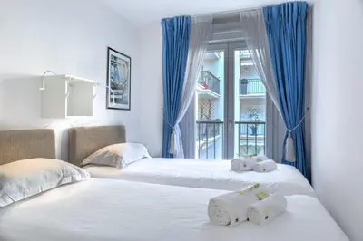 two beds in a room with blue curtains at IMMOGROOM - 3min from beach - AC - 10min from Palais - Wifi in Cannes
