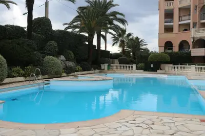 a large blue swimming pool with palm trees and a building at Appartement Palm d'Azur in Cannes