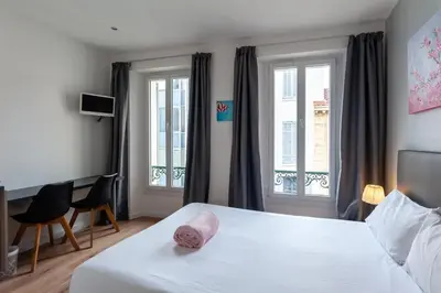 a bedroom with a white bed and two windows at Hotel l'Hotera in Cannes
