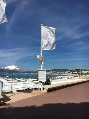 two flags on a pole next to the beach at Appartement Le Palais Des Iles in Cannes