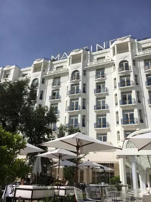 a large white building with tables and umbrellas in front of it at Appartement Le Palais Des Iles in Cannes