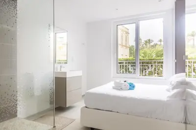 a white bedroom with a bed and a window at PLAGE Ground floor apartment on seafront with large terrace in Cannes