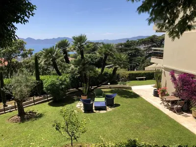 a garden with chairs and palm trees and a building at Appartement - villa Le Saint Georges avec superbe jardin et vue mer panoramique in Cannes