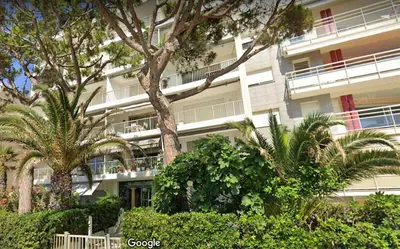 a white building with palm trees in front of it at Fettolina Palm Beach, Location Cannes front de mer et plage in Cannes