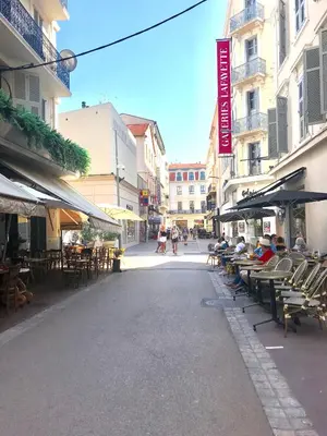 a street with tables and chairs and people sitting in chairs at 24 Août Sucquet in Cannes