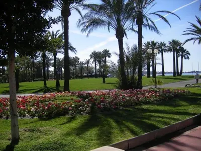 a park with flowers and palm trees and a sidewalk at Karolina Properties - Appartement Commodore Croisette in Cannes