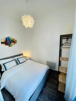 a bedroom with a white bed and a chandelier at Deux pièces proche Palais et plages in Cannes
