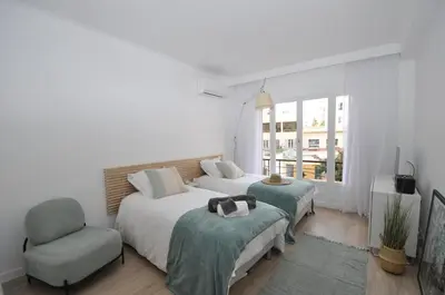 a white bedroom with two beds and a chair at 9 Rue Buttura in Cannes