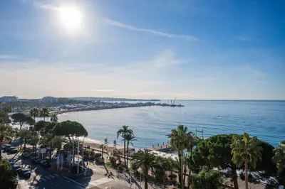 a view of a beach with palm trees and the ocean at REF 1181 - Cannes Croisette - Sea view apartment for rent in Cannes