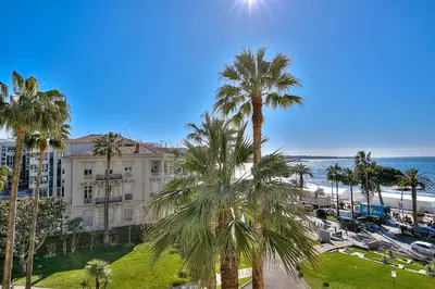 a building with palm trees in front of the ocean at Appartements Croisette Grand Hôtel in Cannes