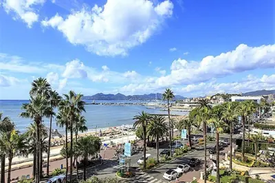a view of a beach with palm trees and cars at Appartements Croisette Grand Hôtel in Cannes