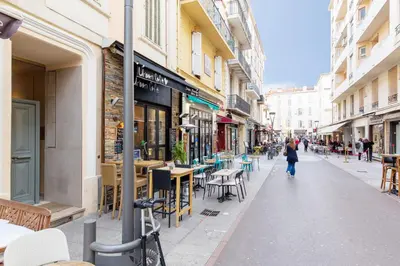 a woman walking down a street with tables and chairs at L'Albion YourHostHelper in Cannes