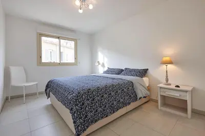 a white bedroom with a bed and a window at Appartement Résidence Montaigne in Cannes