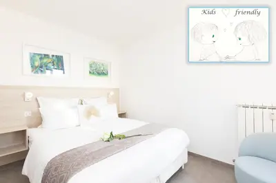 a white bedroom with a bed and a blue chair at On la Croisette: luxe 2 bedrooms/ 2 baths in Cannes