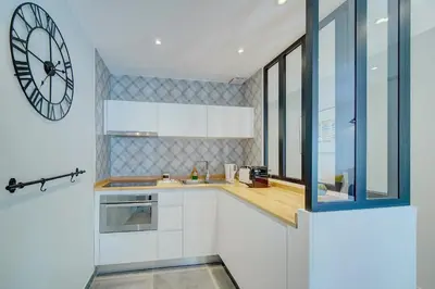 a kitchen with white cabinets and a large clock on the wall at IMMOGROOM - AC - 5min from the beaches 8 min from Palais in Cannes