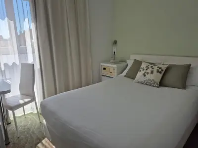a bedroom with a white bed with a chair and a window at Hôtel Ligure in Cannes