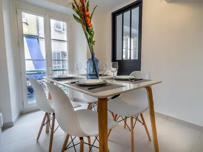 a dining room table with white chairs and a vase with flowers at Appartement centre de Cannes in Cannes