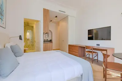 a bedroom with a white bed and a desk and a television at La Guitare 23 - Large modern studio with balcony in center of Cannes, just behind Grand Hotel in Cannes