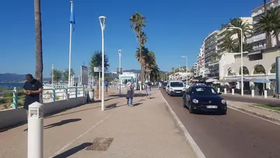 a person walking down a sidewalk next to a street with cars at CLEM SOLEIL in Cannes