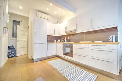 a kitchen with white cabinets and a wooden floor at Cannes Carré d'Or Cozy 1 BR balcony, Croisette Palais 2 mn by Olam Properties in Cannes