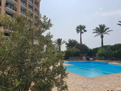 a swimming pool next to a building with palm trees at L'Estérel in Cannes