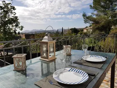 a glass table with plates and glasses on a balcony at A little Eden in Le Cannet