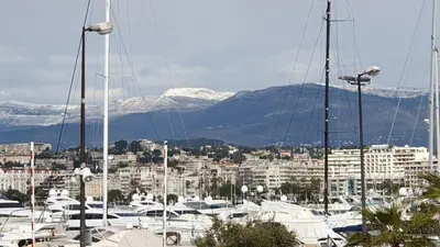 a group of boats docked in a harbor with snow covered mountains at LES MOUETTES A in Cannes