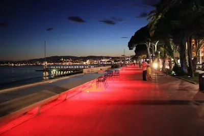a red lighted sidewalk next to the water at night at Beautiful modern apartment in the heart of Cannes in Cannes