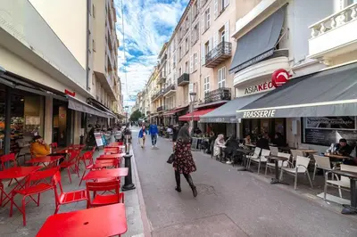a woman walking down a street with red chairs and tables at Beautiful and cozy apartment in the heart of Cannes in Cannes