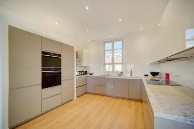 a large kitchen with white cabinets and a wooden floor at IMMOGROOM - Magnificent 180m duplex apartment - Parking - Air conditioning in Cannes