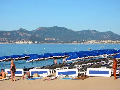 a beach with blue umbrellas and people on the beach at Cannes Plage in Cannes