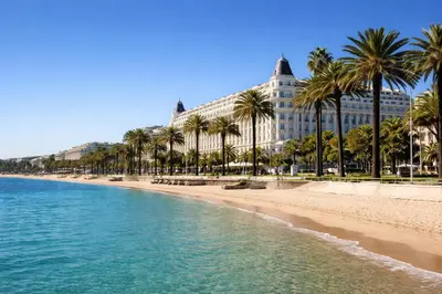 a beach with palm trees in front of a building at Studio chic rénové à 5 min du Palais & de la Croisette Cannes in Cannes