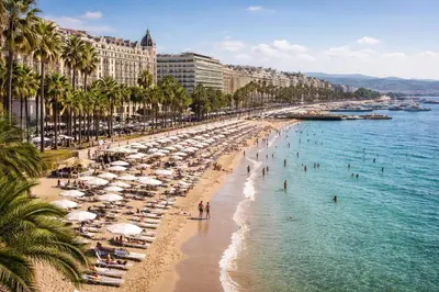 a beach with umbrellas and people in the water at Studio chic rénové à 5 min du Palais & de la Croisette Cannes in Cannes