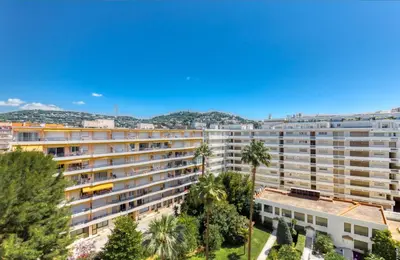 an apartment building with palm trees and mountains in the background at Cannes Croisette Majestic Miramar in Cannes