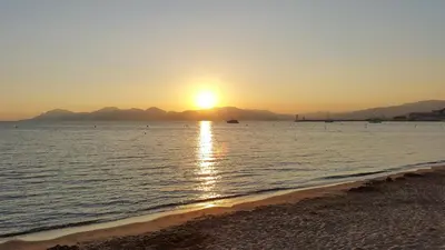 a sunset on the beach with a boat in the water at Appartement Cannes à quelques pas de la mer, de la Croisette et du Palais des Festivals in Cannes