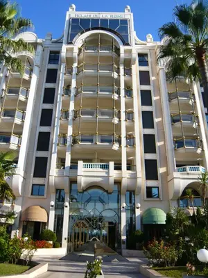 a large white building with palm trees in front of it at Appartement Relais de la Reine Cannes Croisette in Cannes