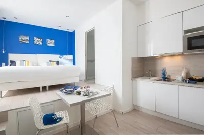 a kitchen with white cabinets and a table and a bed at O Carré Croisette Cannes in Cannes